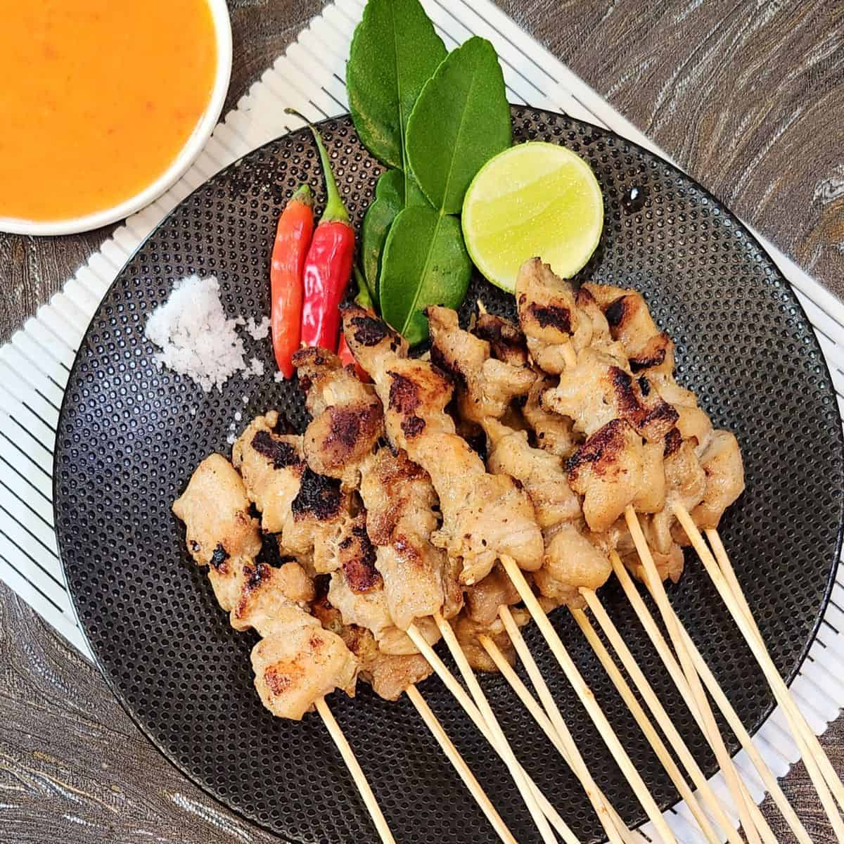A plate of Sate Taichan with chili, a pinch of salt, and lime wedge.