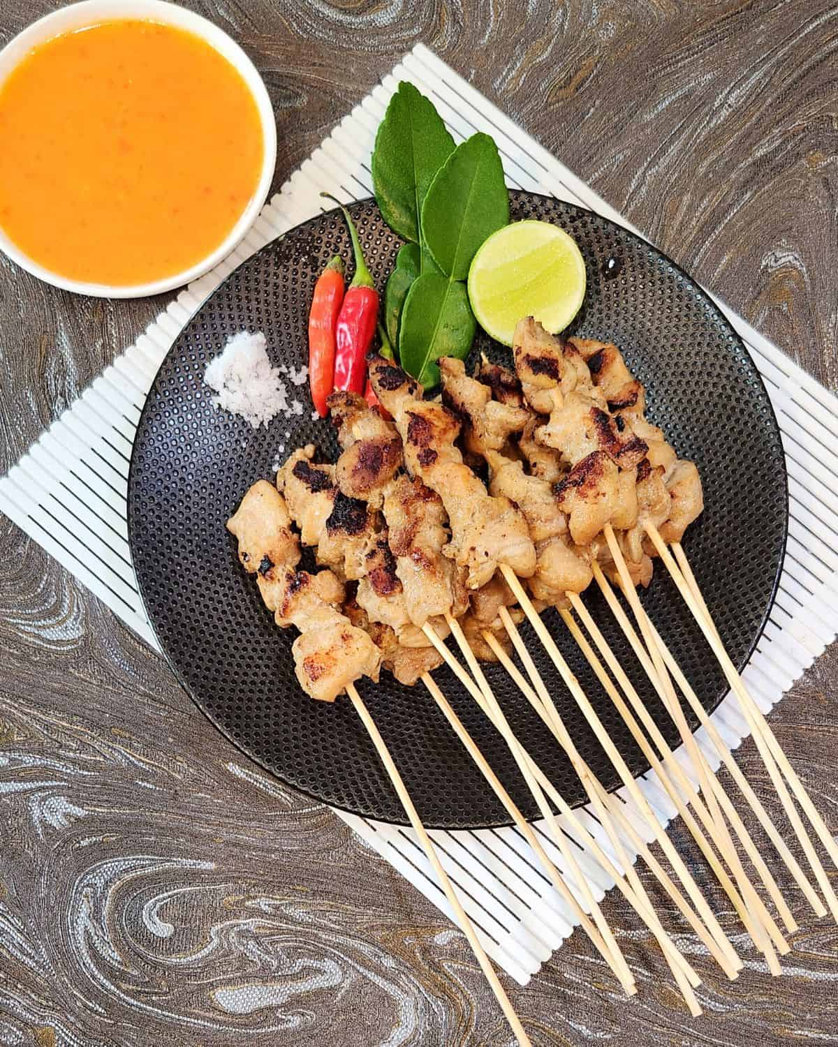 Sate Taichan on a black plate with chili, lime wedge, and sambal next to it.