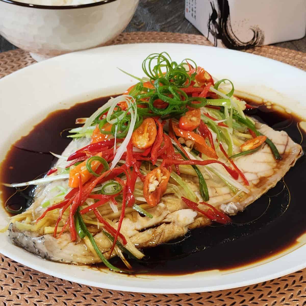Cantonese steamed fish on a plate, garnished with ginger, scallion, and red chili.
