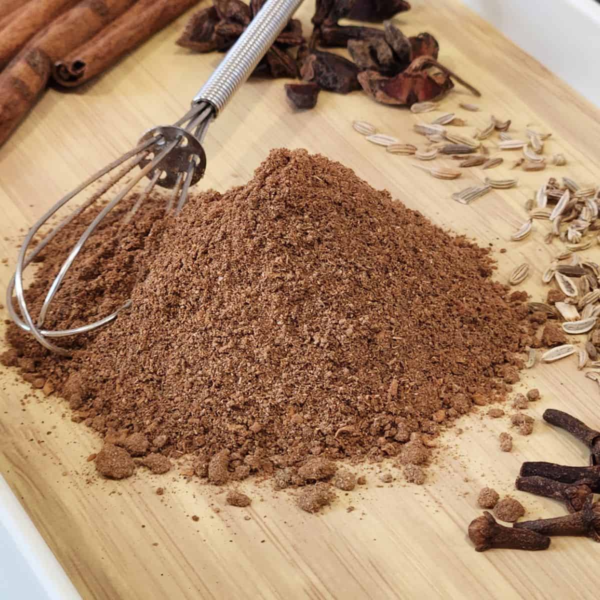 A stack of Chinese five spice powder on a tray with a small whisk.