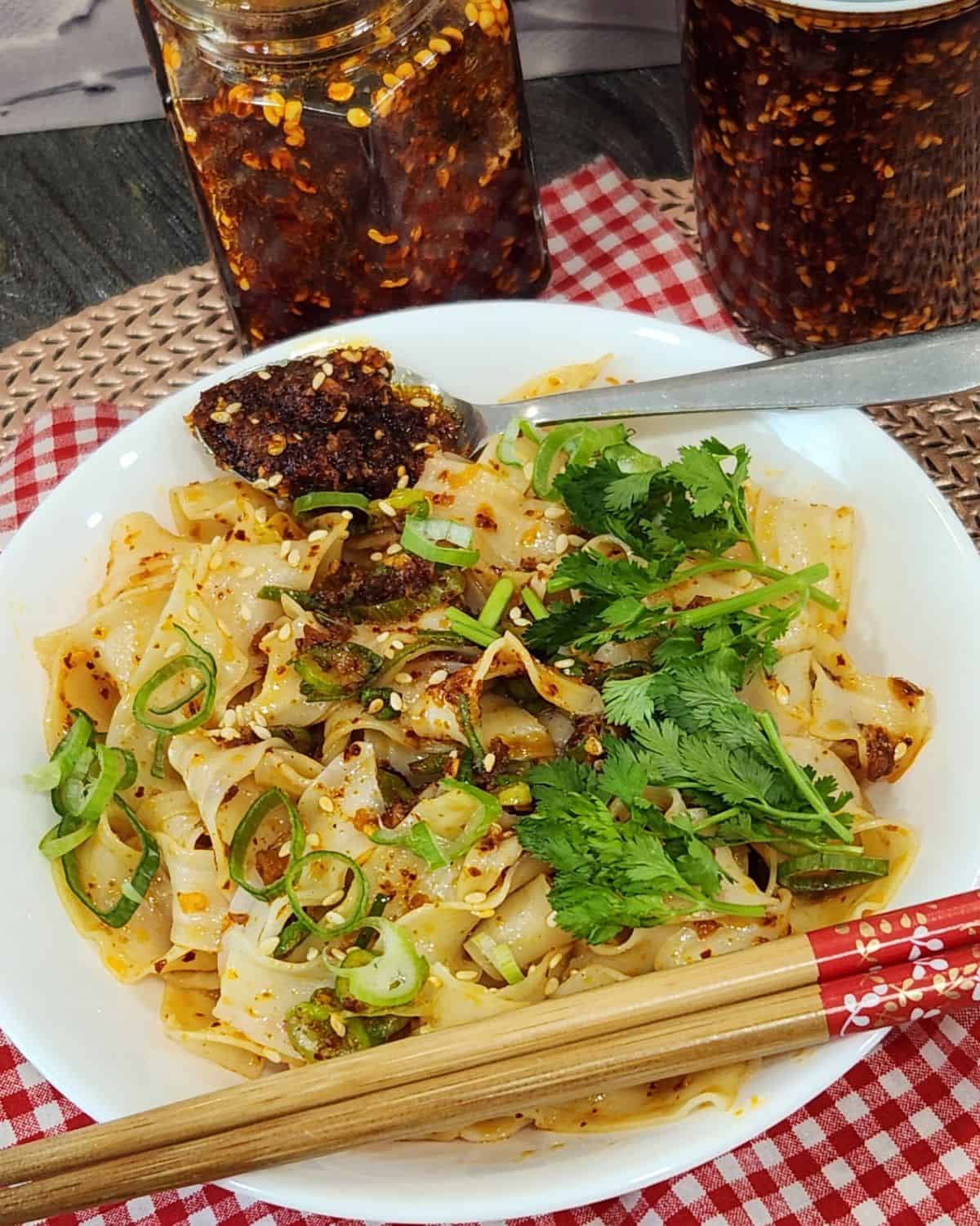 A bowl of garlic chili oil noodles garnished with green onion, cilantro, and sesame seeds.