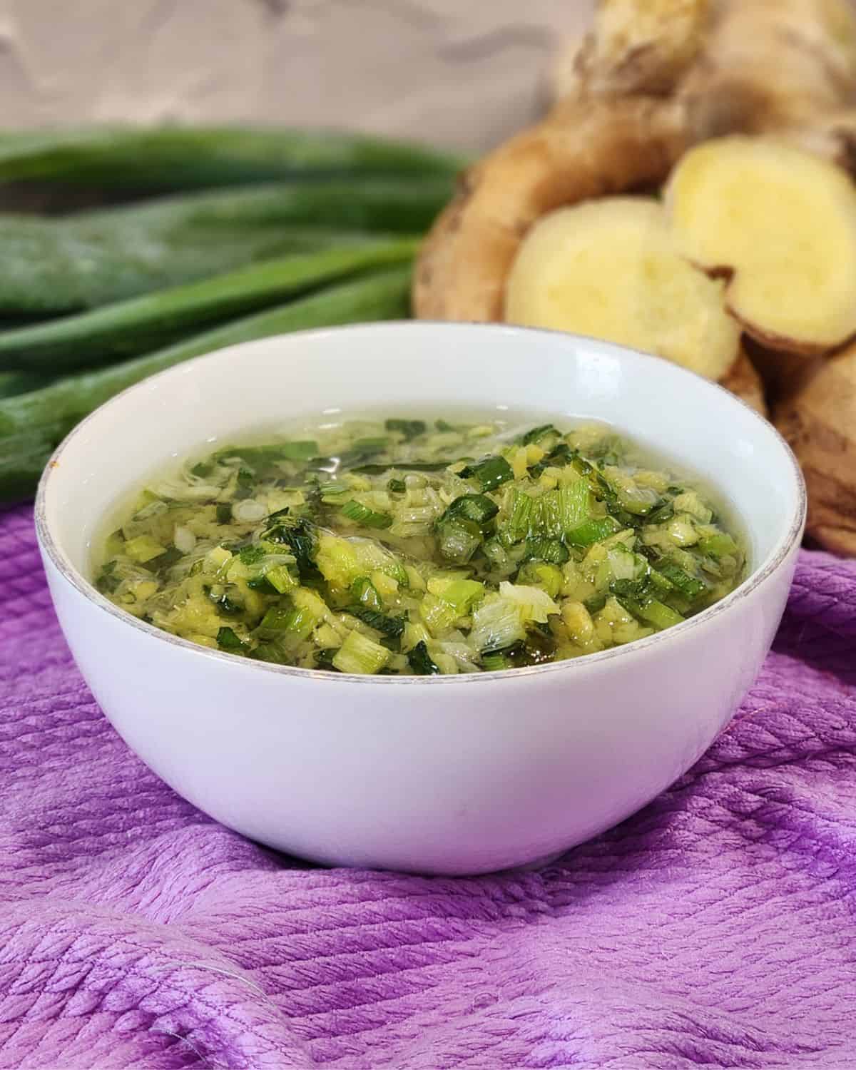 Ginger scallion sauce in a white bowl with fresh scallion and ginger at the back.