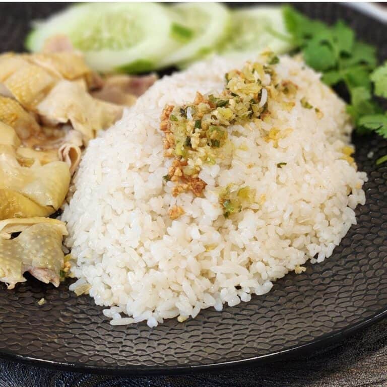 Hainanese chicken rice on a plate, sprinkled with ginger scallion sauce on top.