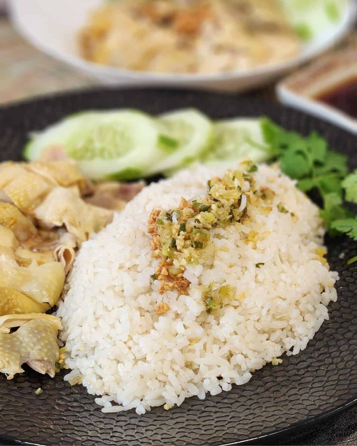 Hainanese chicken rice on a plate with garlic scallion sauce on top and poached chicken.