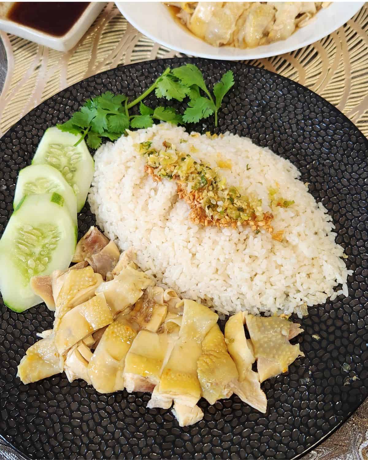 Hainanese Chicken Rice with poached chicken, cucumber slices, cilantro leaves, and sprinkled with ginger scallion sauce.