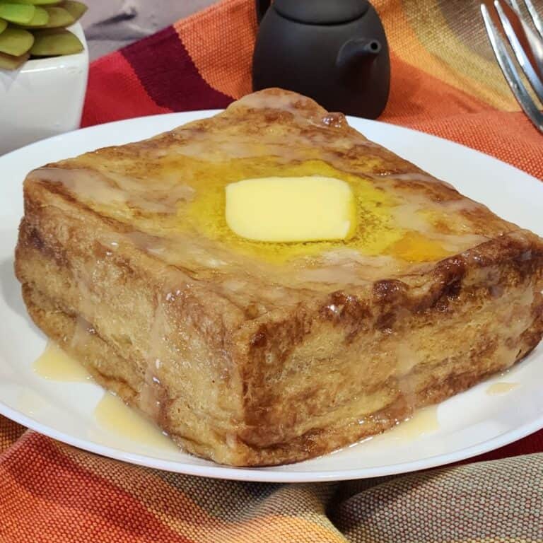 Hong Kong French toast on a white plate, topped with a slice of butter and drizzled with condensed milk and golden syrup.