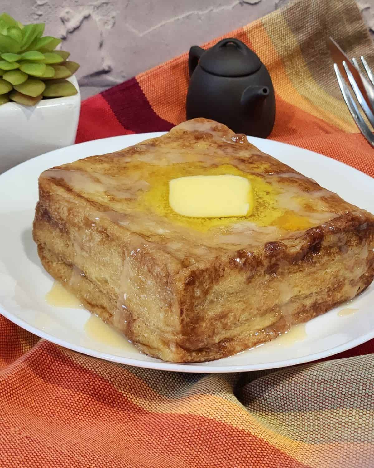 Hong Kong French toast on a white plate, topped with a slice of butter and drizzled with condensed milk and golden syrup.