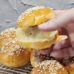 A hand holding one mini burger bun sliced open.