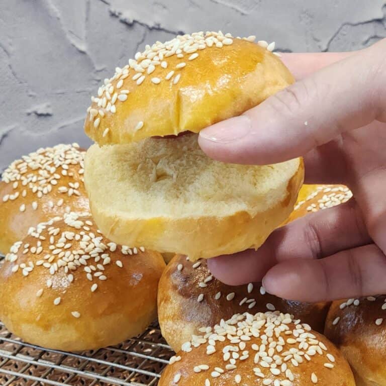 A hand holding one mini burger bun sliced open.