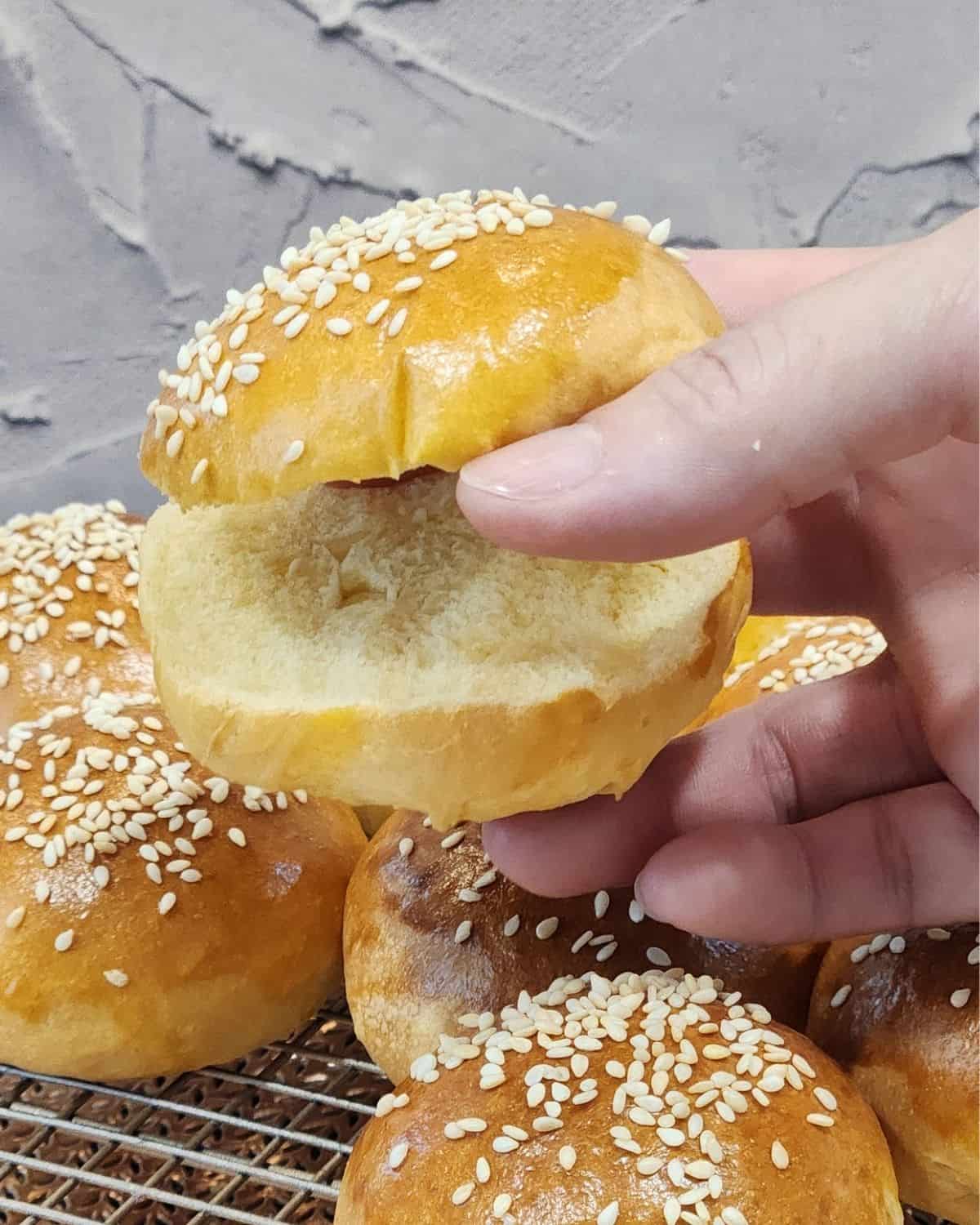 A hand holding one mini burger bun sliced open.