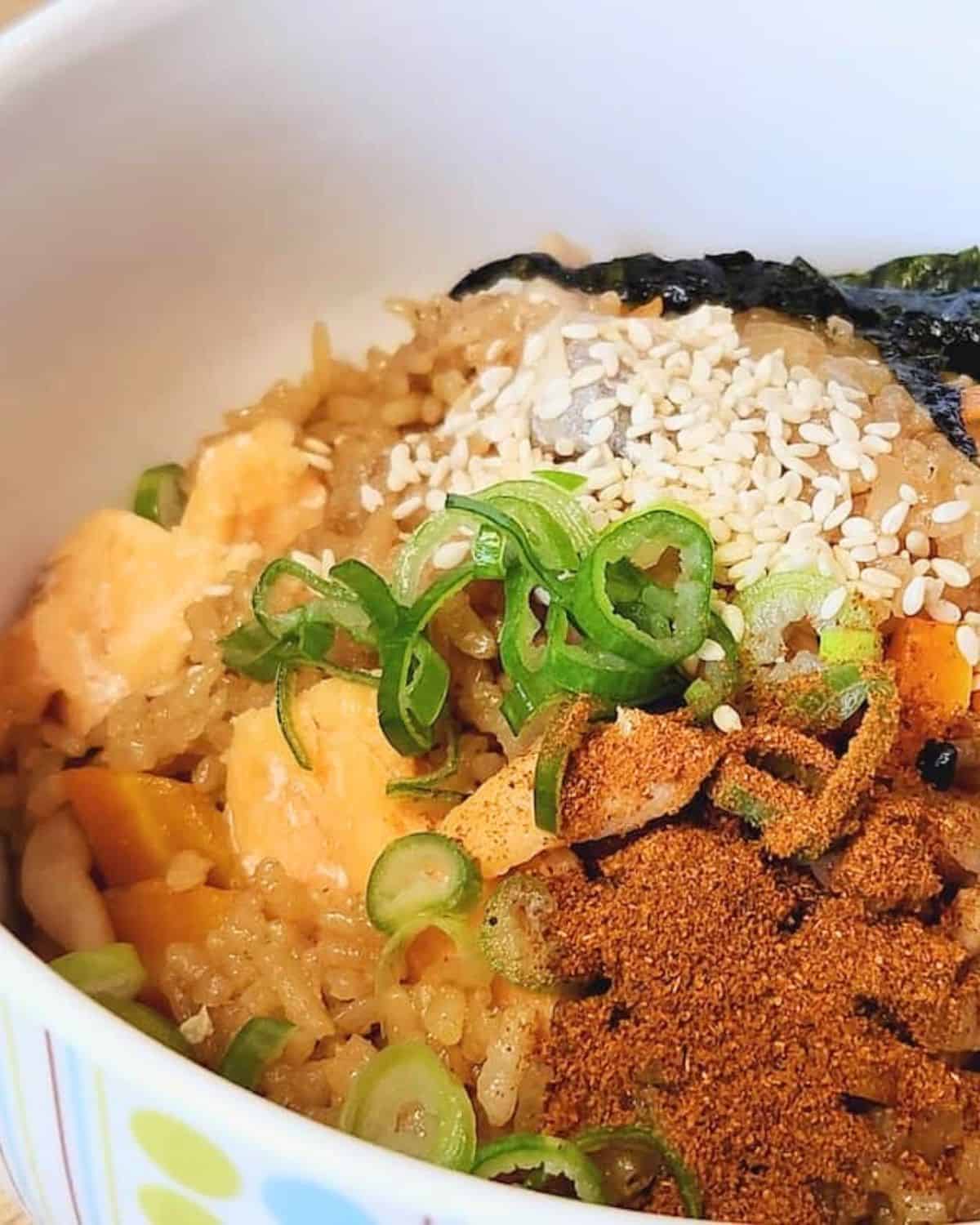 A bowl of salmon takikomi gohan with chili flakes, sesame seeds, and green onion.