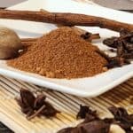 Aromatic speculaas spice mix featuring cinnamon sticks, cloves, and ground spices on a white plate, ideal for baking and cooking.