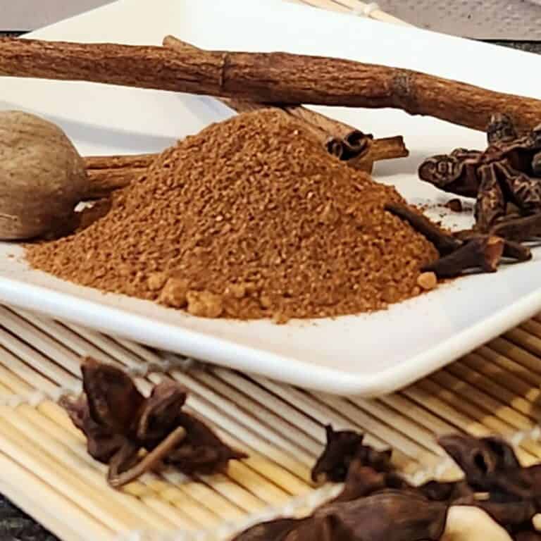 Aromatic speculaas spice mix featuring cinnamon sticks, cloves, and ground spices on a white plate, ideal for baking and cooking.