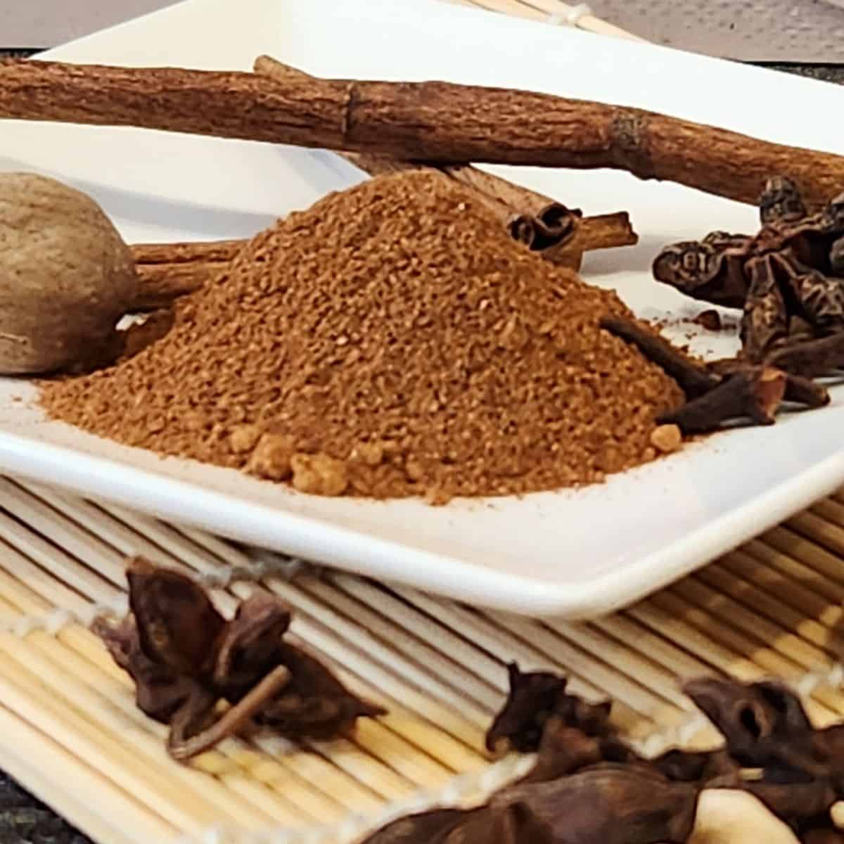 Aromatic speculaas spice mix featuring cinnamon sticks, cloves, and ground spices on a white plate, ideal for baking and cooking.