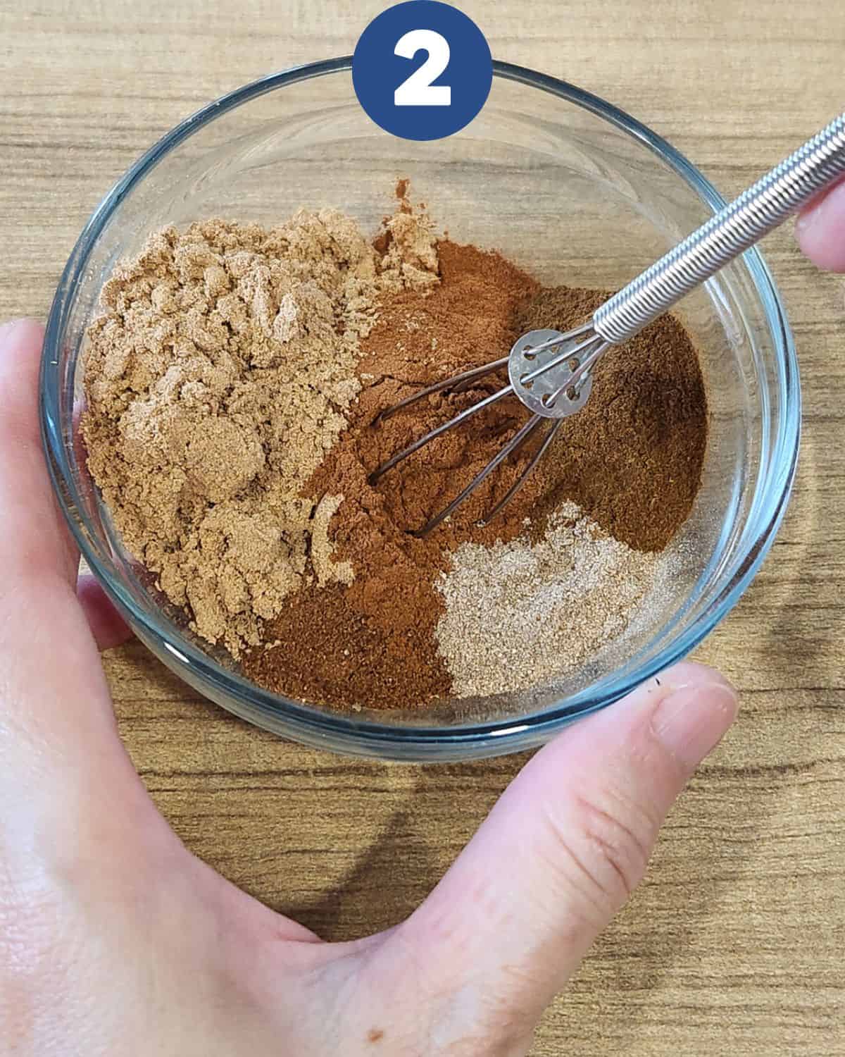 Stirring spekkoek spice in a bowl with a small whisk. 