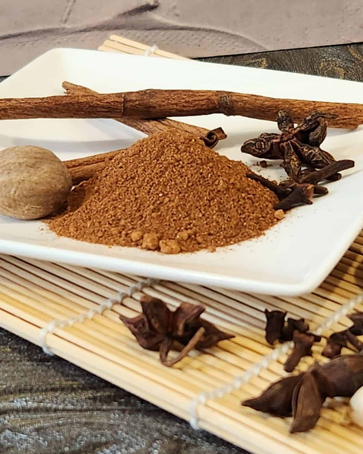 Aromatic speculaas spice mix featuring cinnamon sticks, cloves, and ground spices on a white plate, ideal for baking and cooking.