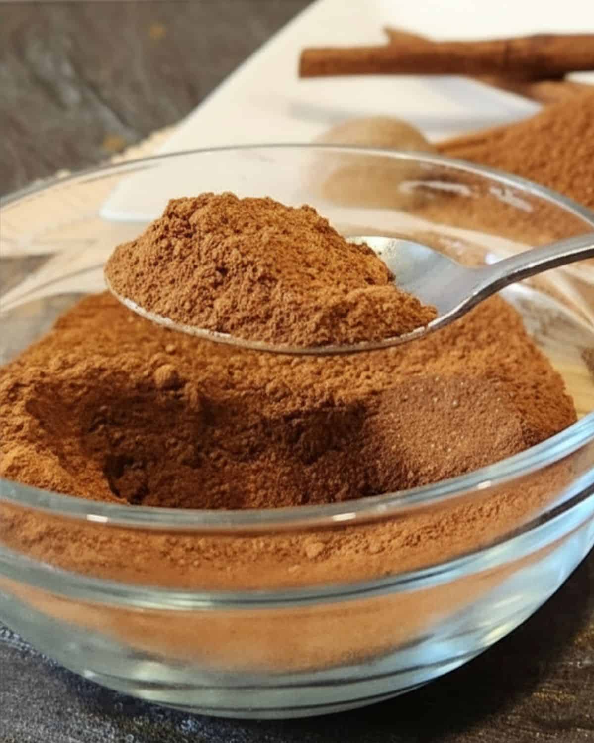 Aromatic Dutch spice mix featuring cinnamon sticks, cloves, and ground spices on a white plate, ideal for baking and cooking.