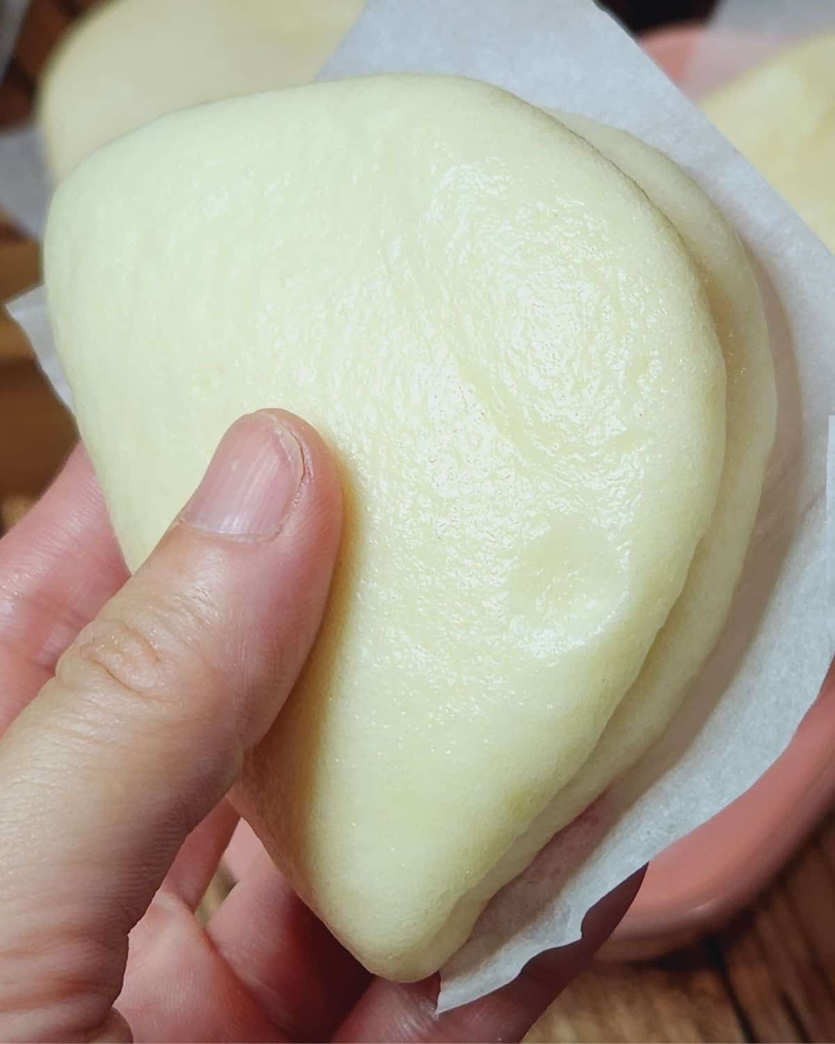 A hand holding a piece of fluffy bao buns.