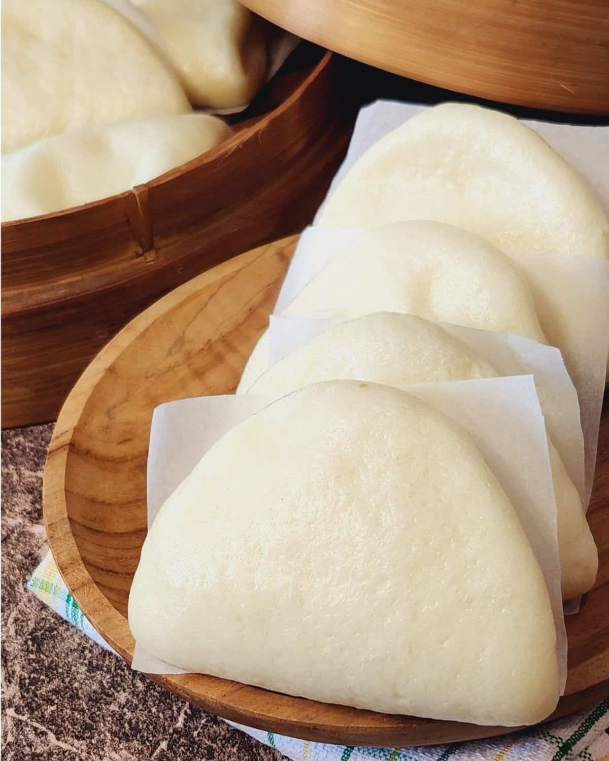 Several freshly steamed bao buns on a wooden plate.