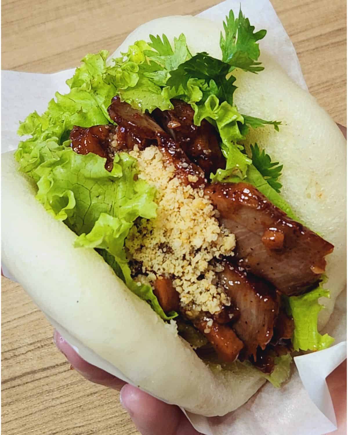 A hand holding gua bao buns with char siu pork inside.