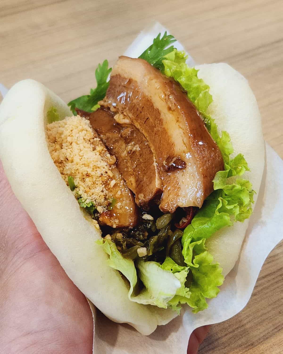A hand holding gua bao buns with braised pork belly inside.