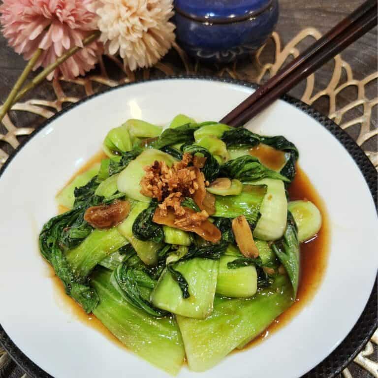 A white plate full of bok choy stir fry garnished with fried garlic.