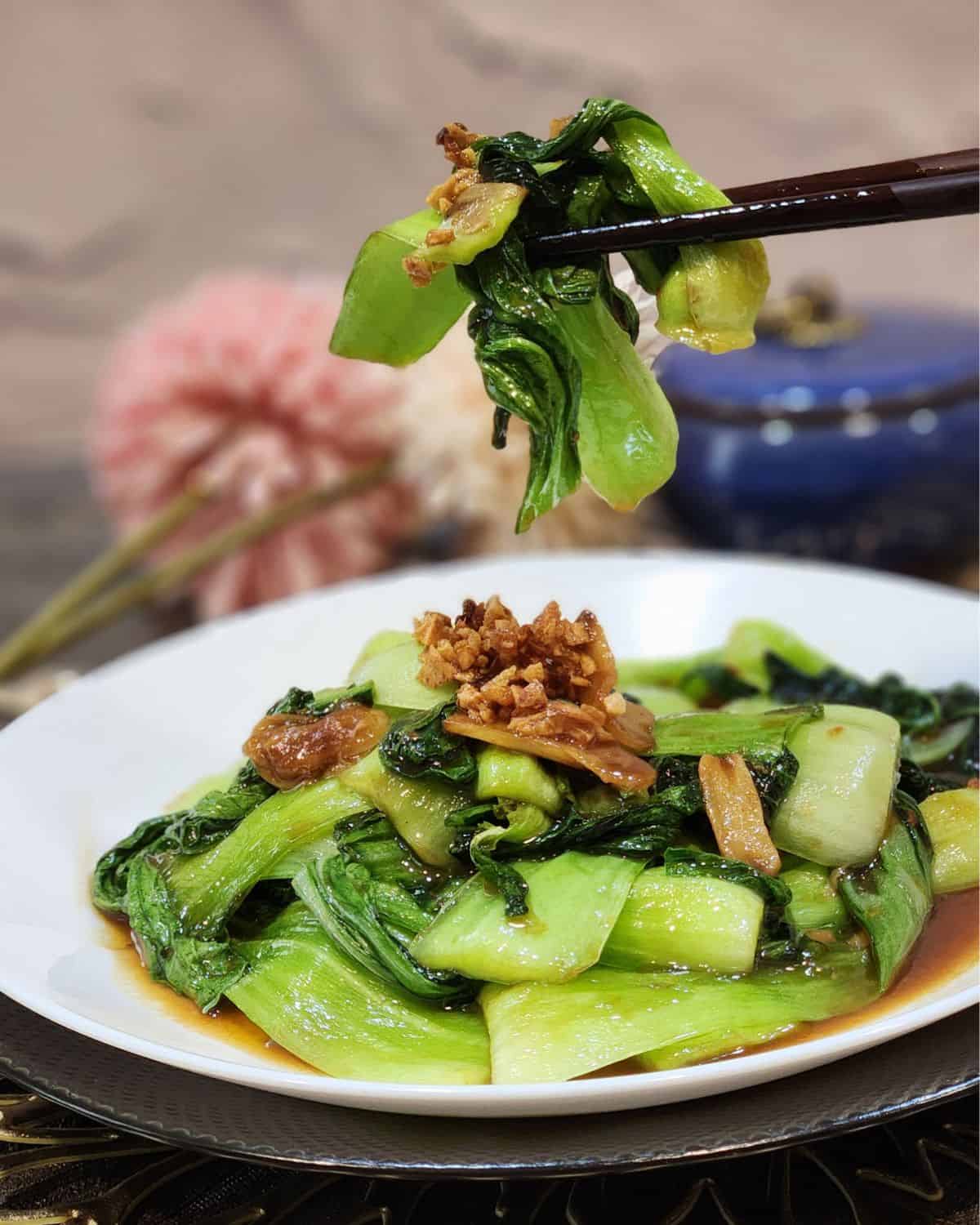 A pair of chopsticks holding bok choy stir fry.