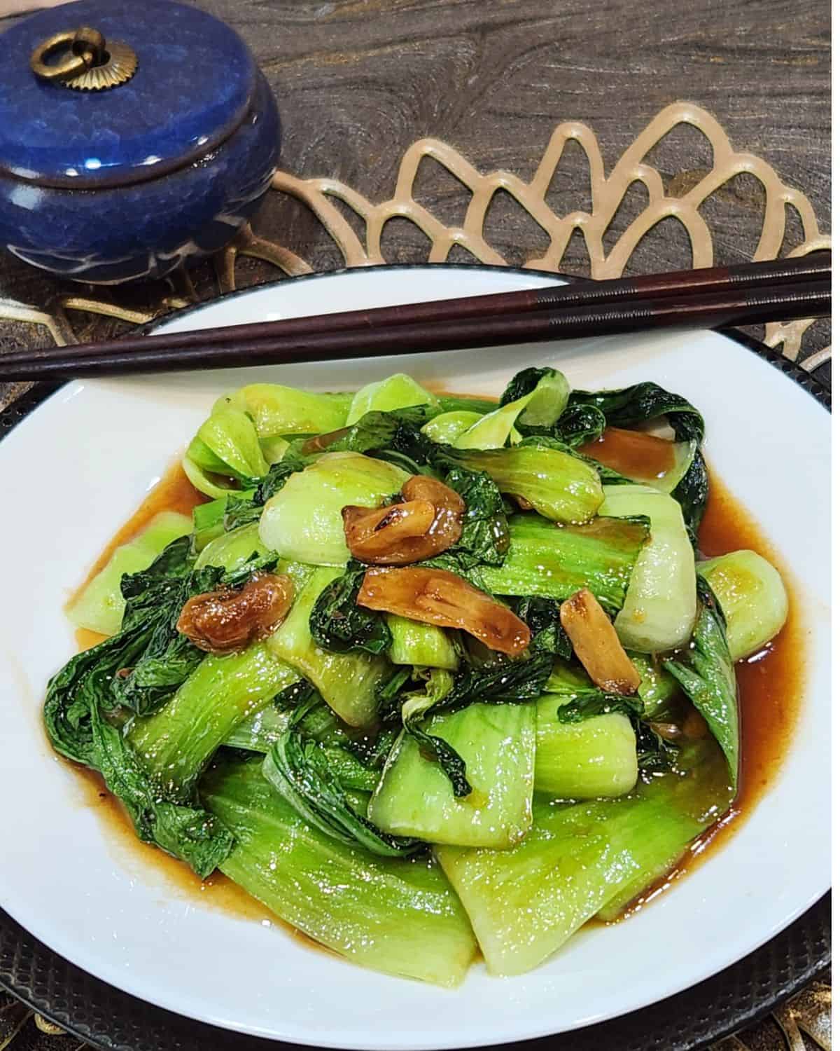 A plate of bok choy stir fry with a pair of chopsticks.