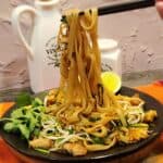 A pair of chopsticks holding chicken pad thai.