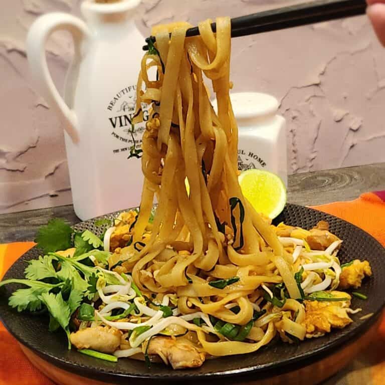 A pair of chopsticks holding chicken pad thai.