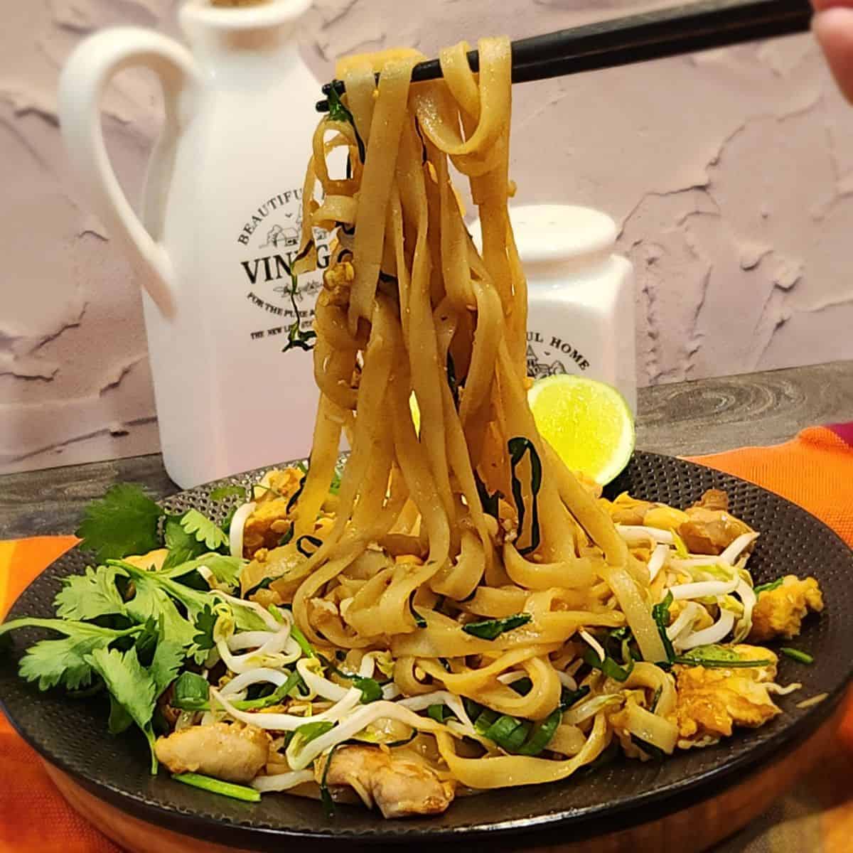 A pair of chopsticks holding chicken pad thai.