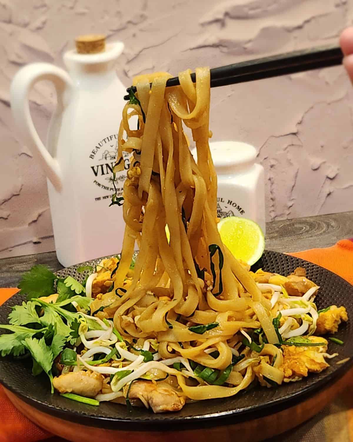 A pair of chopsticks holding chicken pad thai.