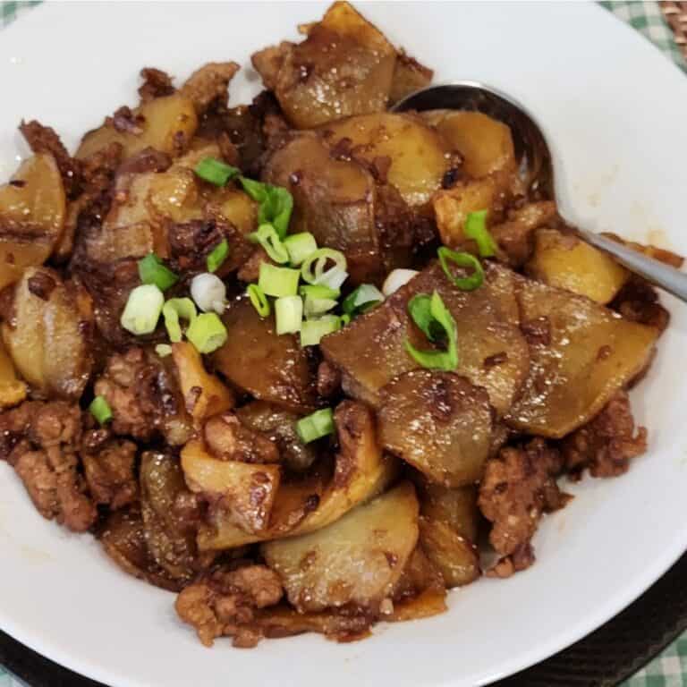 A plate of ground pork stir fry with potatoes, garnished with green onion.