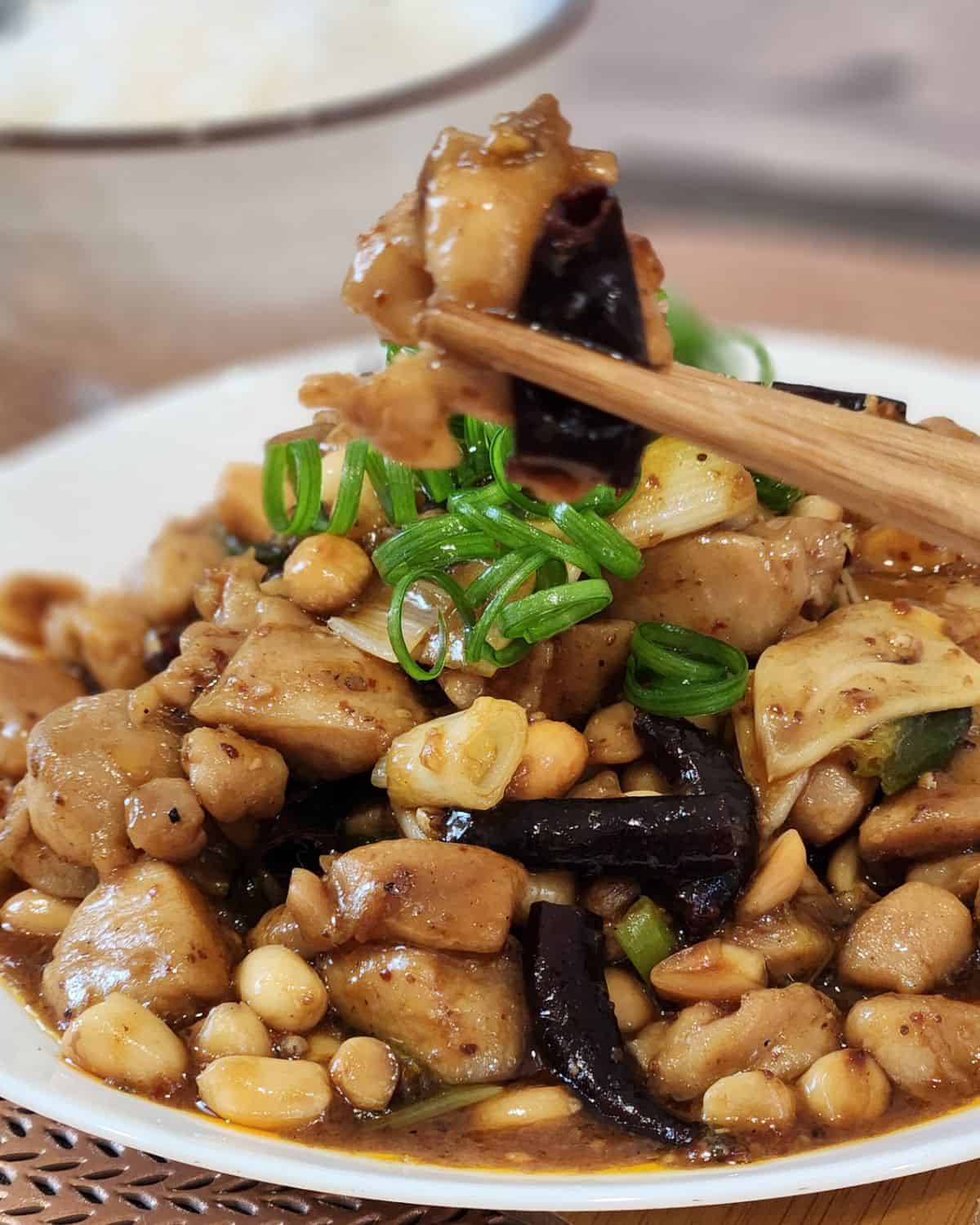 A pair of chopsticks holding kung pao chicken.