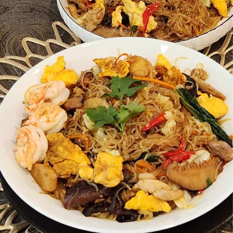 A plate of stir fried glass noodles with chicken, shrimp, and vegetables.