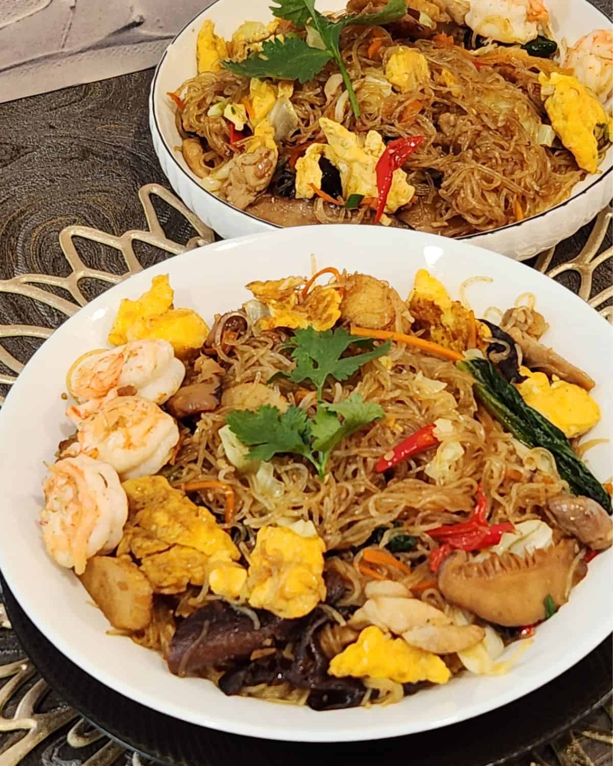 A plate of stir fried glass noodles with chicken, shrimp, and vegetables.