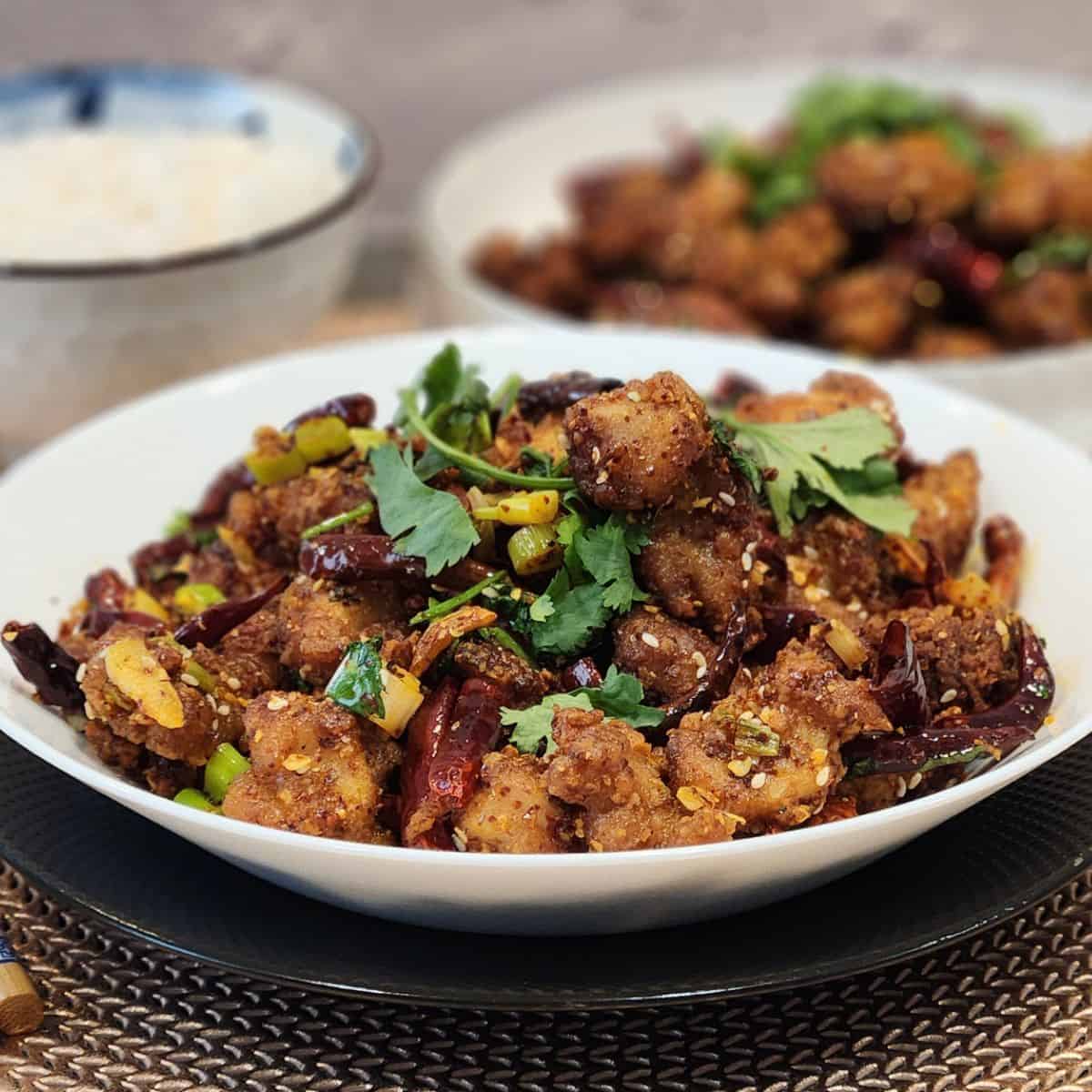 A white serving plate with Szechuan chicken dish in it, garnished with cilantro leaves.