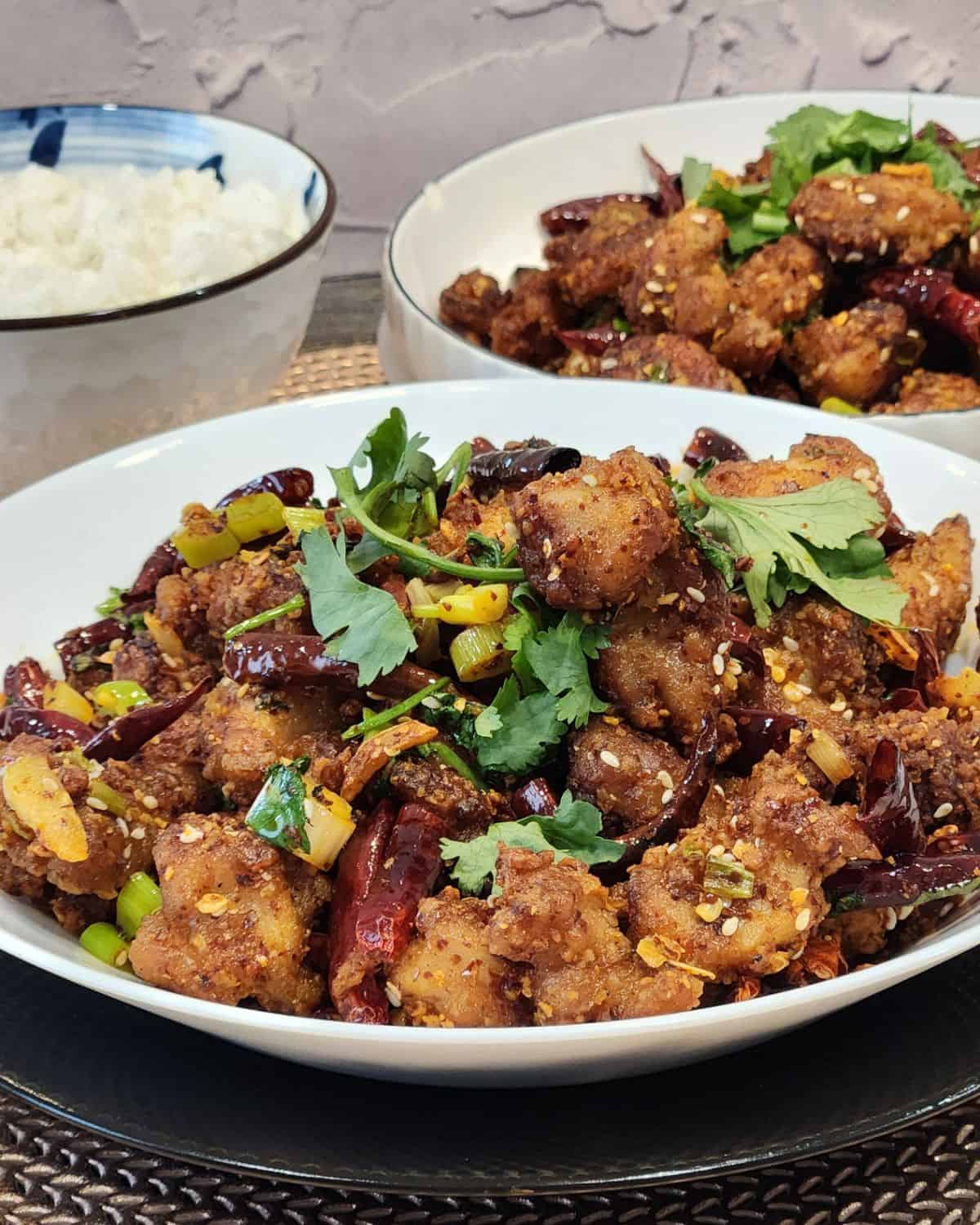 A white serving plate with Szechuan chicken dish in it, garnished with coriander leaves.