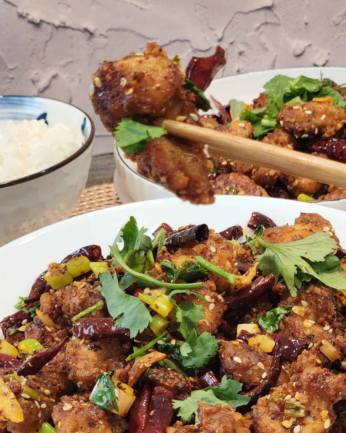 A pair of chopsticks holding Szechuan chicken.