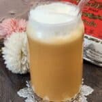 A glass of Thai iced tea with frothed milk on top.