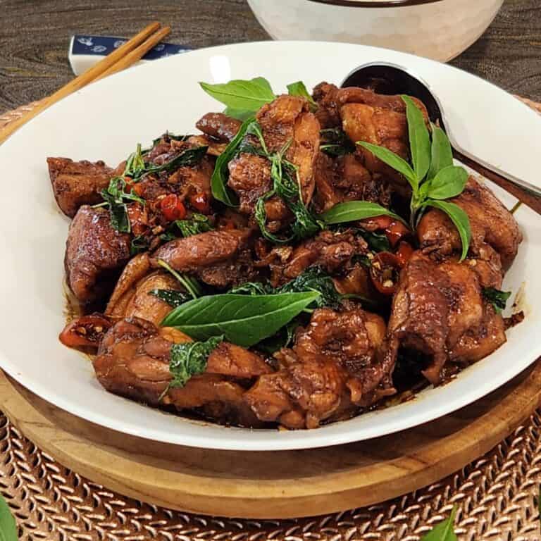 A plate of Taiwanese three cup chicken with Thai basil leaves and chilis.