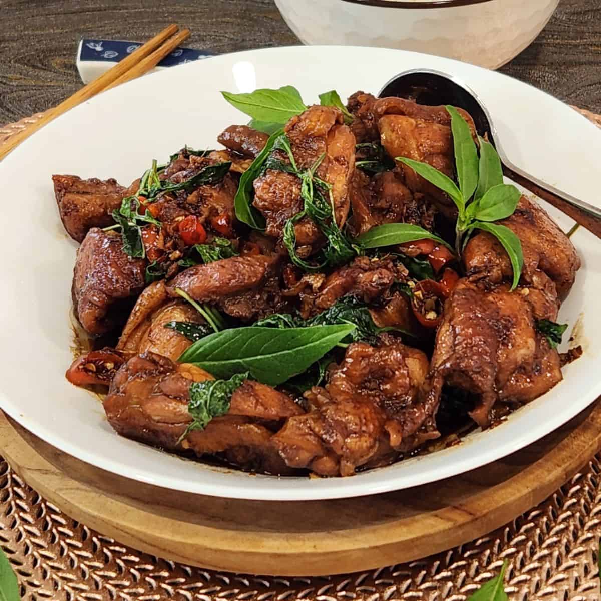 A plate of Taiwanese three cup chicken with Thai basil leaves and chilis.