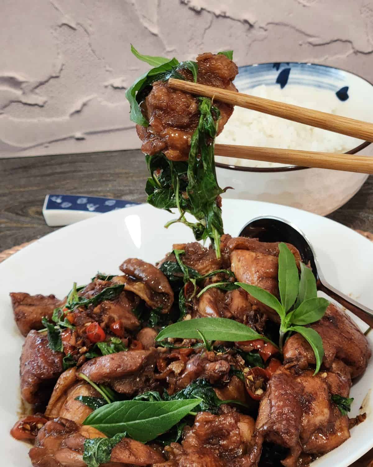A pair of chopsticks holding three cup chicken pieces.