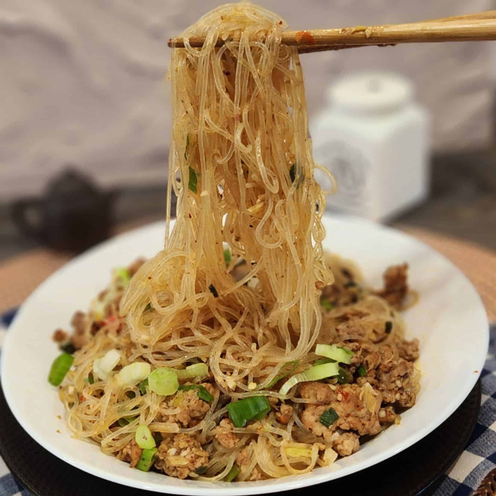 A pair of chopsticks holding ants climbing a tree glass noodles.