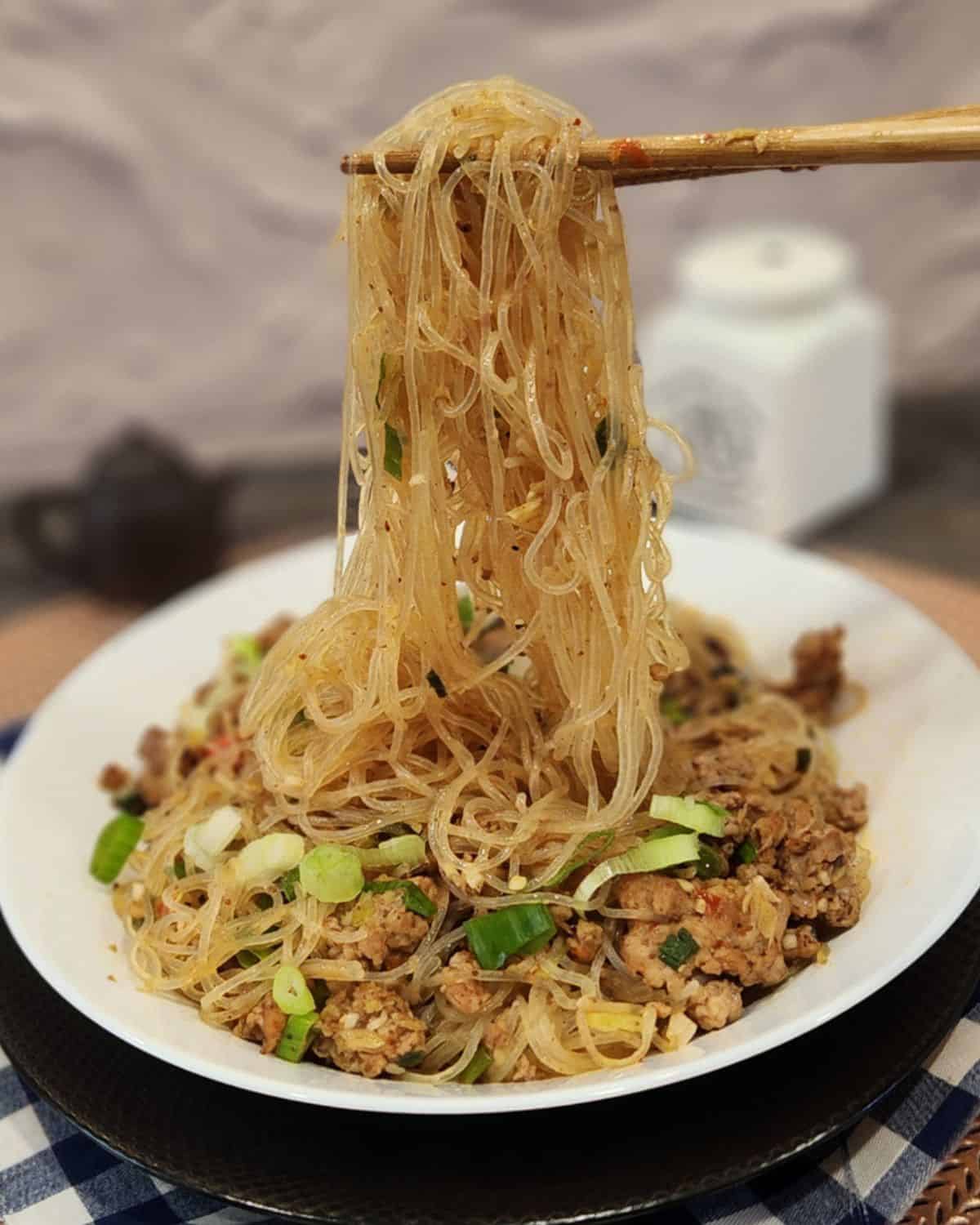 A pair of chopsticks holding ants climbing a tree glass noodles.