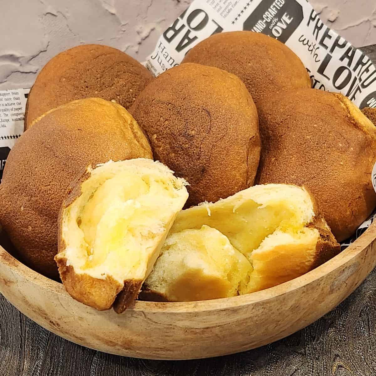 Several coffee bun in a wooden bowl with one torn open to reveal butter filling inside.