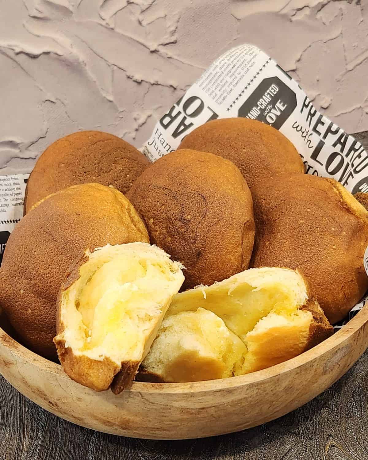 Several coffee buns in a wooden bowl with one bread torn to show salted butter filling.