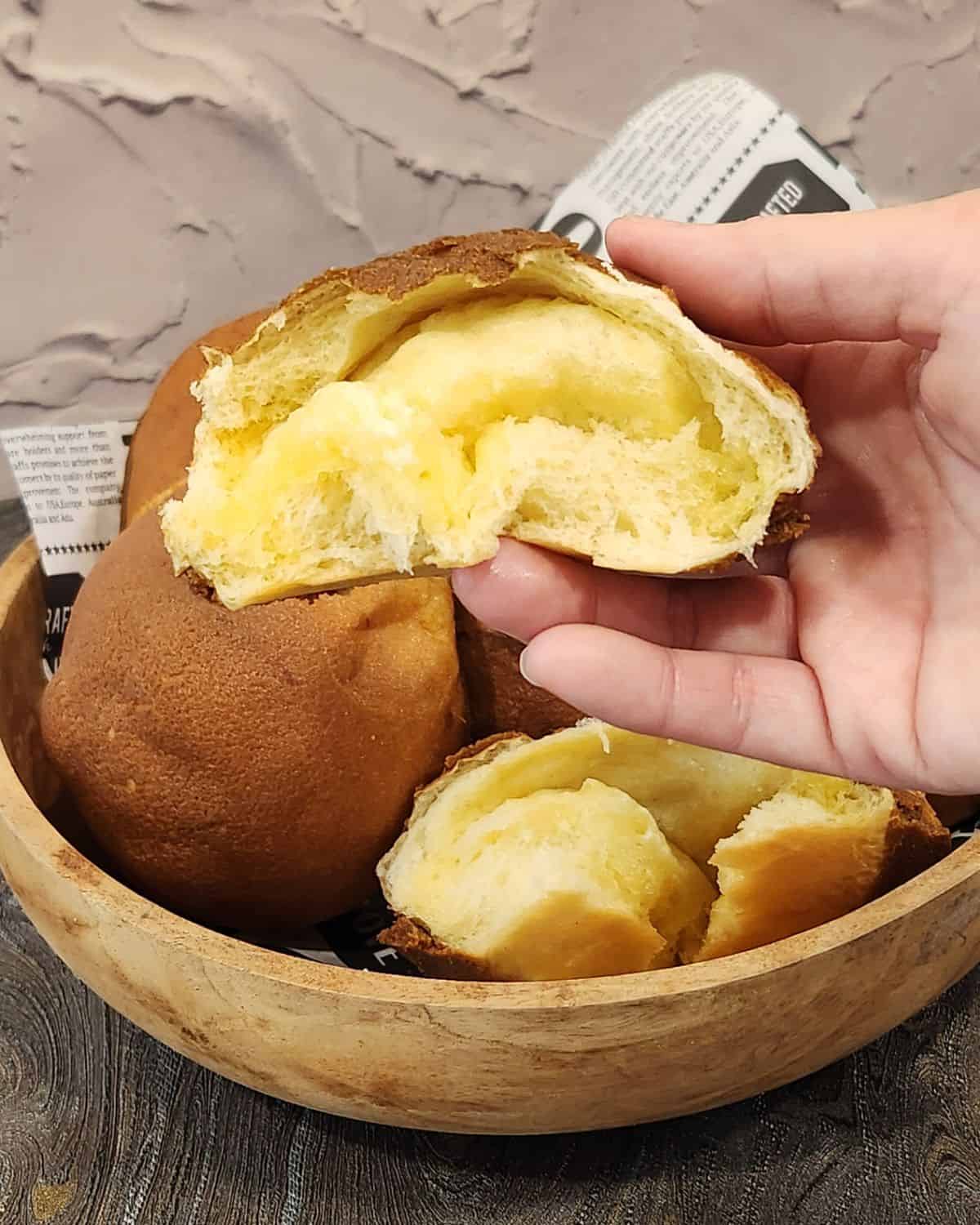A hand holding a coffee bun with melted butter filling.
