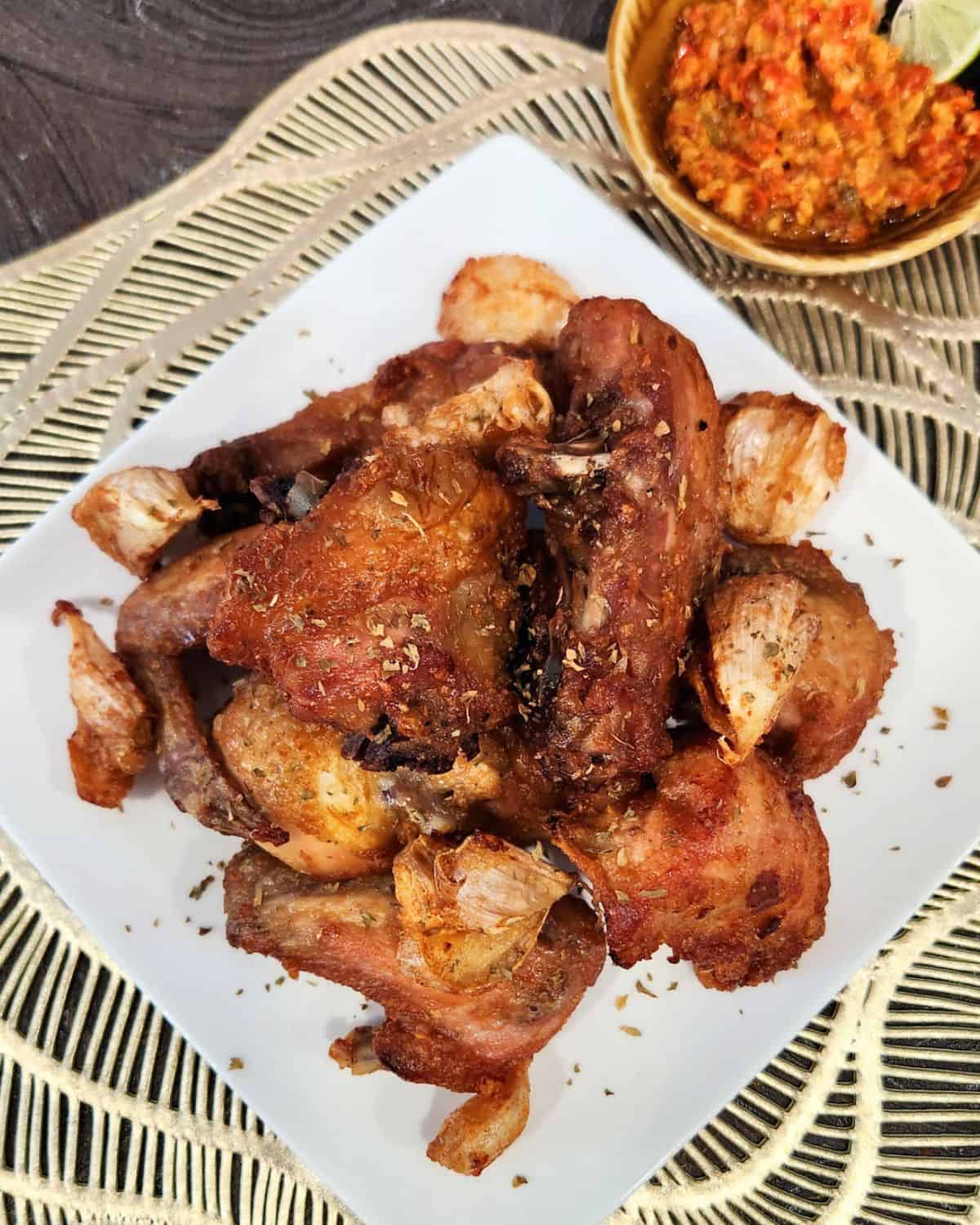 A plate full of garlic fried chicken with a small bowl of chili sauce.
