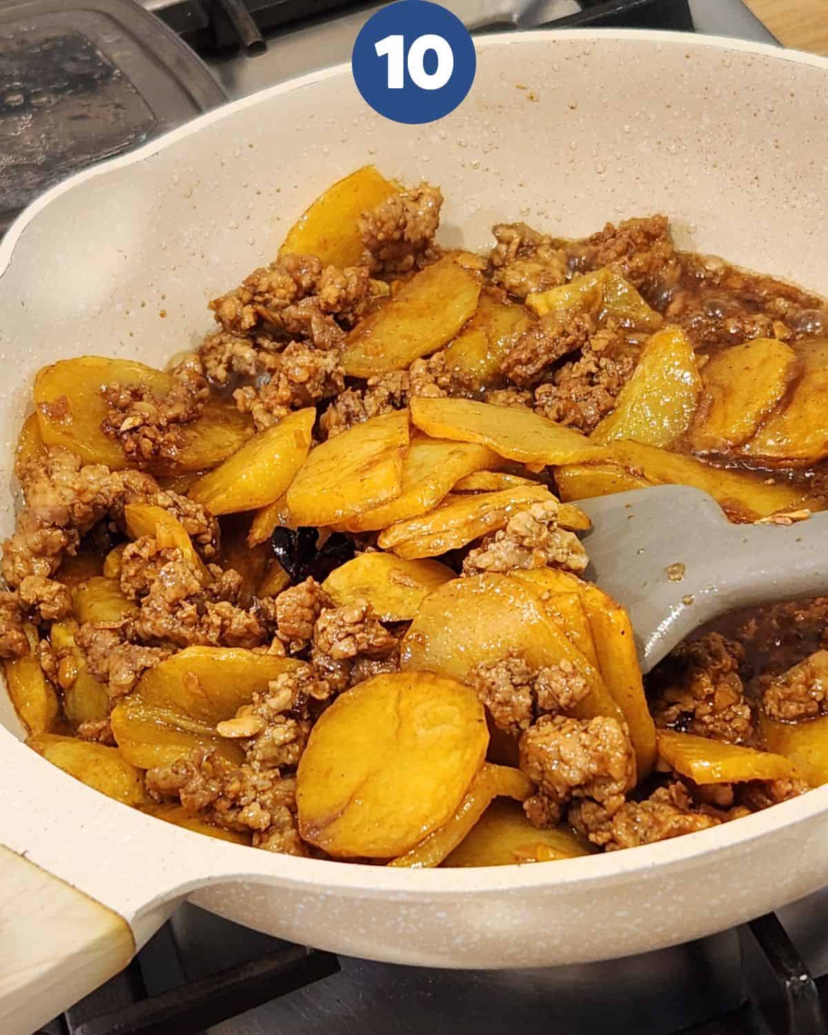 Stir frying the potatoes and ground pork until cooked.